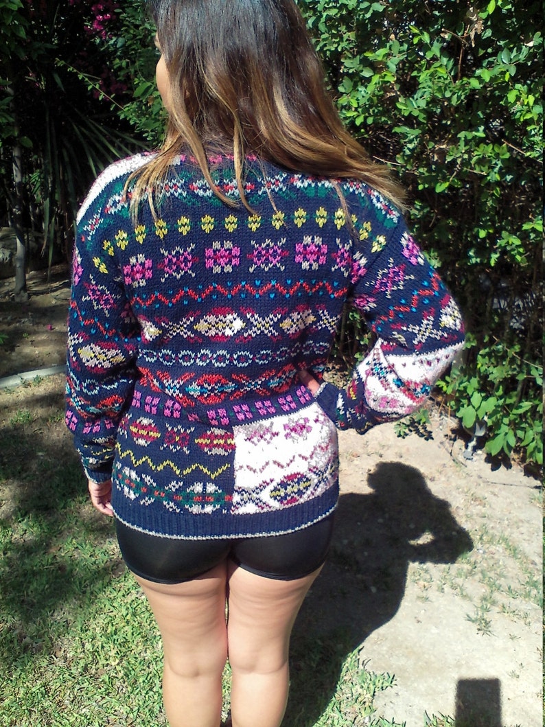 May include: A colorful knitted sweater with a geometric pattern in shades of blue, pink, yellow, and white. The sweater has a loose fit and a crew neck.