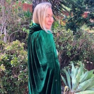 May include: A woman wearing a long, emerald green velvet cape with a high collar. The cape is flowing in the wind and the woman is looking over her shoulder.