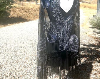 May include: A black sheer shawl with silver embroidery featuring a peacock design. The shawl has fringe along the bottom edge.