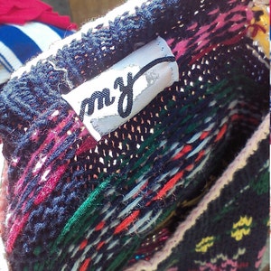 May include: A close-up of a colorful knitted sweater with a white tag that says "m.y." The sweater has a pink, red, green, and blue pattern.