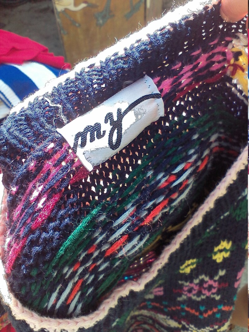 May include: A close-up of a colorful knitted sweater with a white tag that says "m.y." The sweater has a pink, red, green, and blue pattern.