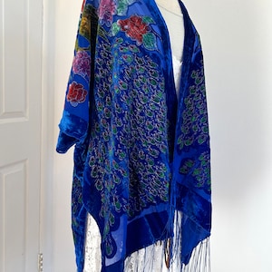 May include: A blue velvet shawl with a peacock design and fringe. The peacock is embroidered with green, gold, and red thread.