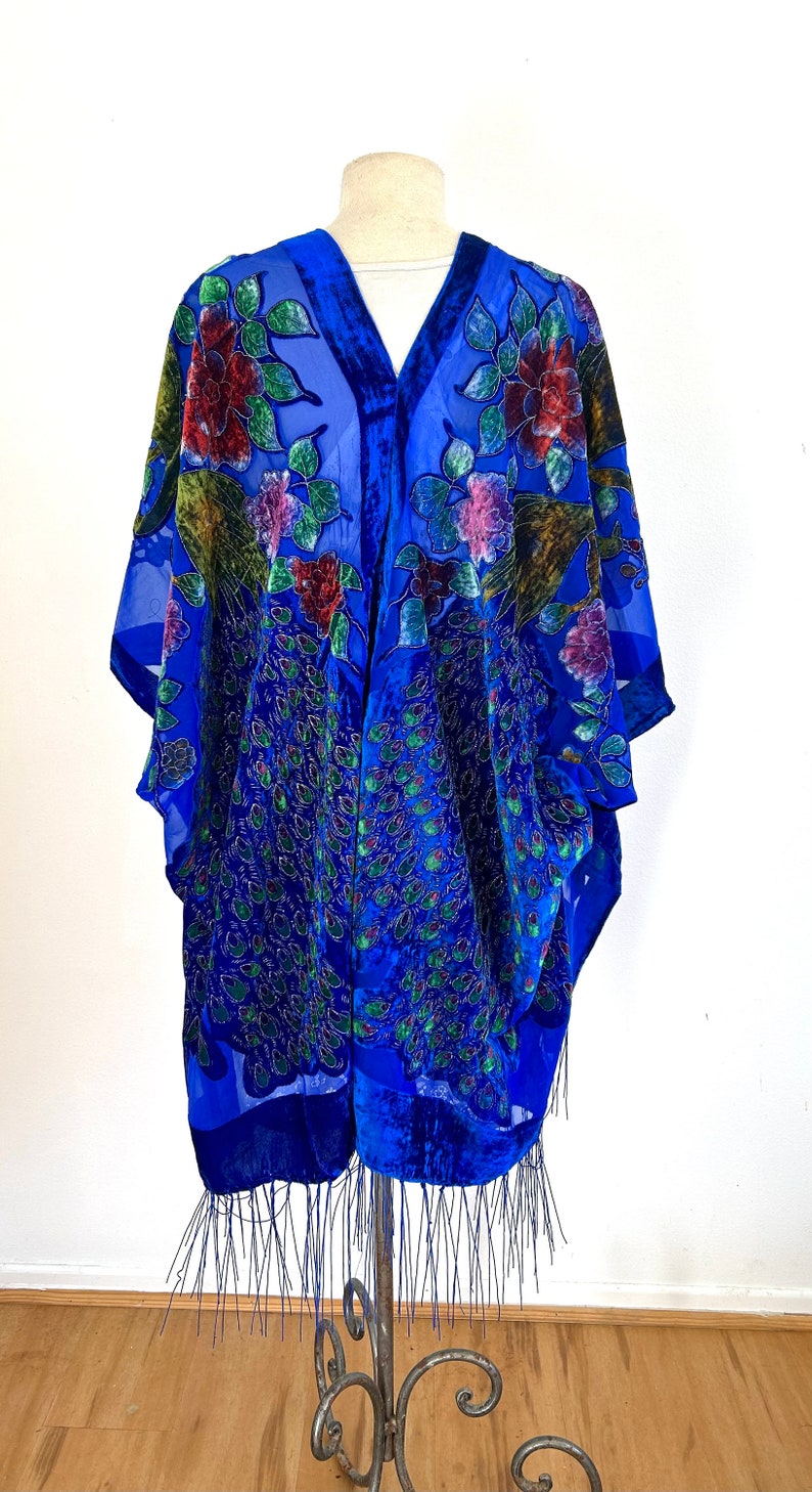 May include: A royal blue velvet shawl with a peacock feather design and floral embroidery. The shawl has a fringe trim and is displayed on a mannequin.
