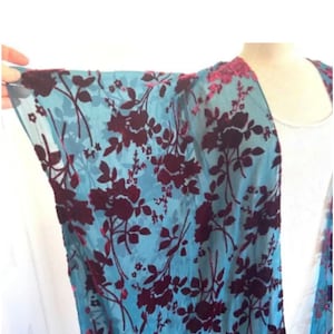 May include: A light blue kimono with a floral pattern in deep burgundy. The flowers and leaves are densely arranged across the fabric. The edges of the garment are trimmed with a darker, textured material.