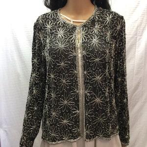 May include: A black beaded jacket with a silver floral pattern. The jacket has a front zip closure and long sleeves.