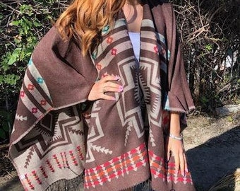 Może przedstawiać: Brązowe poncho z geometrycznym wzorem w odcieniach czerwieni, pomarańczy, błękitu i bieli. Poncho ma frędzle wzdłuż dolnego brzegu.