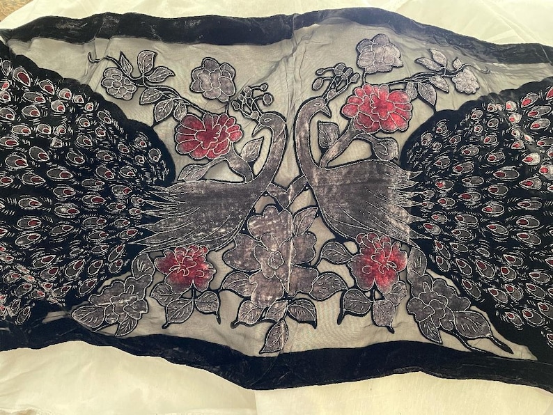 May include: A black and gray textile with a velvet border, featuring two stylized peacocks facing each other. The design includes red and gray floral accents and peacock feather details.