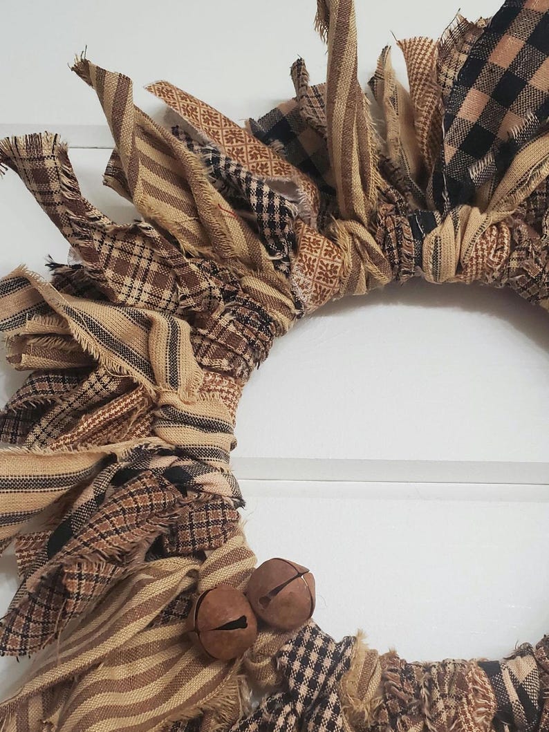 May include: A brown and tan fabric wreath with black and white plaid accents. The wreath is decorated with two small brown bells.