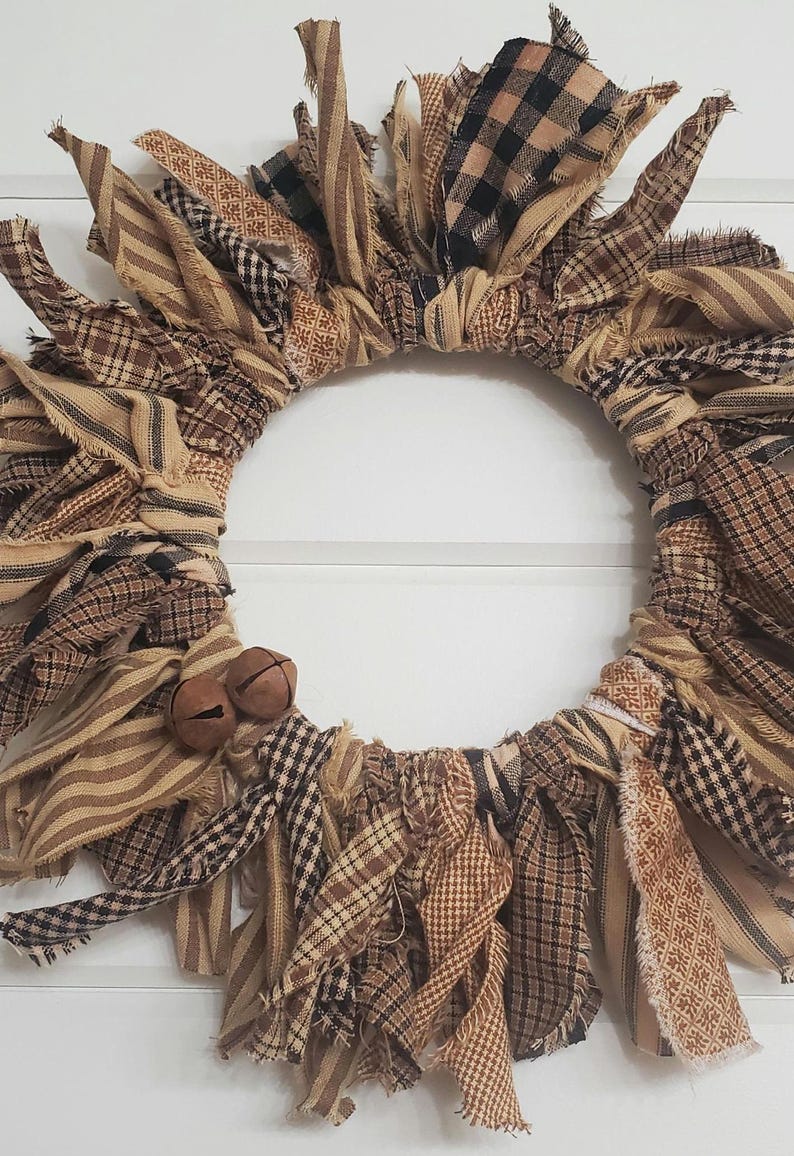 May include: A brown and tan fabric wreath with frayed edges and two small brown bells. The wreath is made of various plaid and striped fabrics.