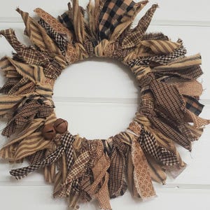May include: A brown and tan fabric wreath with frayed edges. The wreath is decorated with small brown bells.