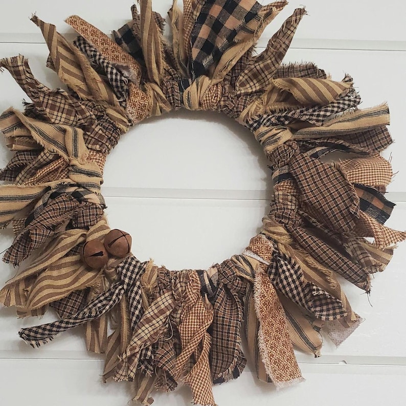May include: A brown and tan fabric wreath with frayed edges. The wreath is decorated with small brown bells.