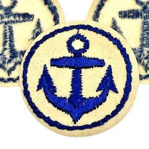 Könnte beinhalten: Ein weißer Stoff-Patch mit einem blauen gestickten Anker-Design. Der Anker hat einen seilartigen Rand.