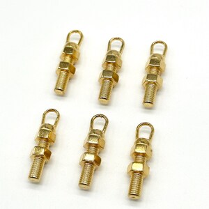 May include: Six gold-toned metal charms shaped like nuts and bolts with a loop at the top.