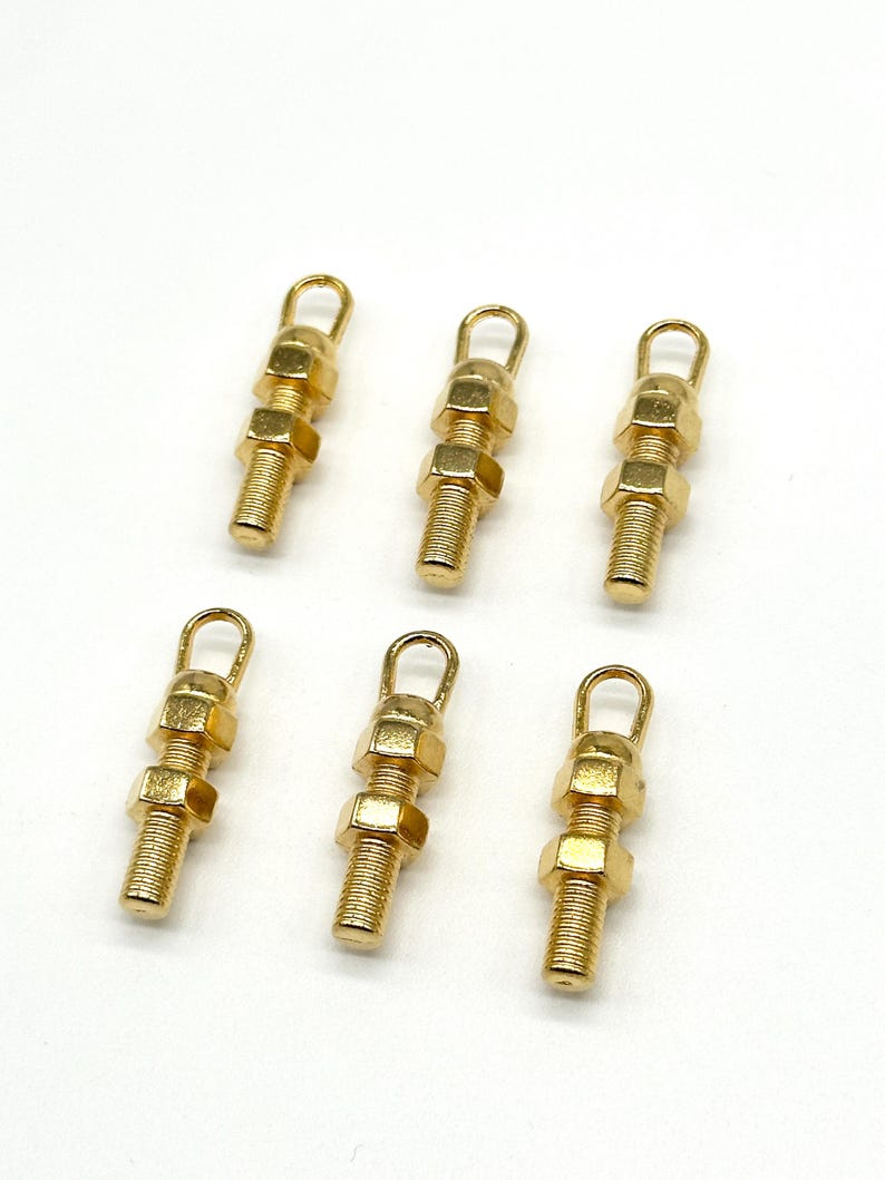 May include: Six gold-toned metal charms shaped like nuts and bolts with a loop at the top.