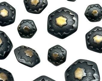 Op de afbeelding: Een verzameling van 11 zeshoekige knopen met een zwarte metalen afwerking en een gouden midden. De knopen hebben een decoratief ontwerp rond de randen.