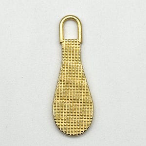 May include: Gold-toned metal zipper pull with a teardrop shape and a textured surface.