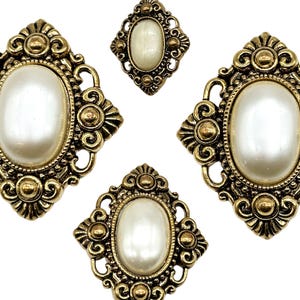 Puede incluir: Conjunto de tres adornos de metal dorado con centros de perla blanca. Los adornos tienen forma de diamante y óvalo.