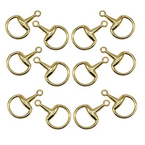 Puede incluir: Nueve anillos de bocado de caballo de color dorado. Cada anillo tiene un pequeño lazo redondo en un lado y un lazo ovalado más grande en el otro. Los anillos están dispuestos en tres filas de tres.