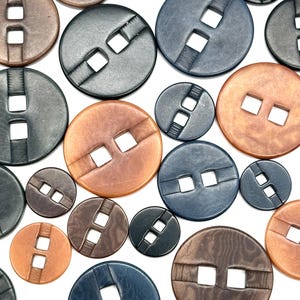 May include: Assortment of round buttons with a double square hole in the center. The buttons are in various colors, including brown, black, and blue.