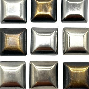 Könnte beinhalten: Neun quadratische Metallknöpfe in drei verschiedenen Ausführungen: Silber, Messing und Antikmessing.