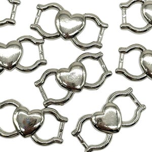 May include: Silver-toned metal heart-shaped clasps with a wavy design. These clasps are perfect for jewelry making or adding a touch of elegance to your crafts.