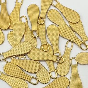 May include: A pile of gold-colored zipper pulls with a textured surface. The pulls are shaped like teardrops with a loop at the top.
