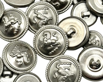 May include: A group of silver metal buttons with a raised design of a winged lion. The buttons have a shank on the back for sewing.