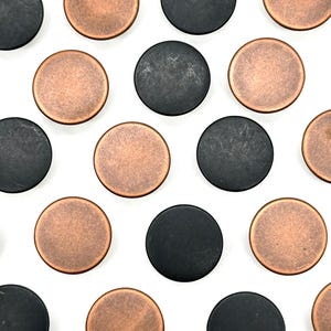 May include: A collection of round, copper and black buttons. The buttons are arranged in a repeating pattern.