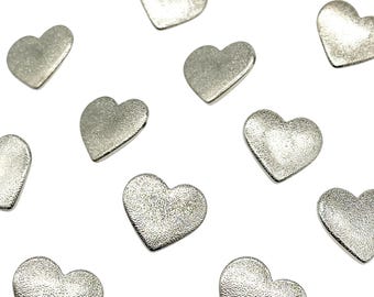 May include: Scattered silver-colored heart-shaped embellishments with a textured surface. These small, metallic hearts are scattered across a white background. Ideal for crafting, scrapbooking, or adding a touch of romance to various projects.