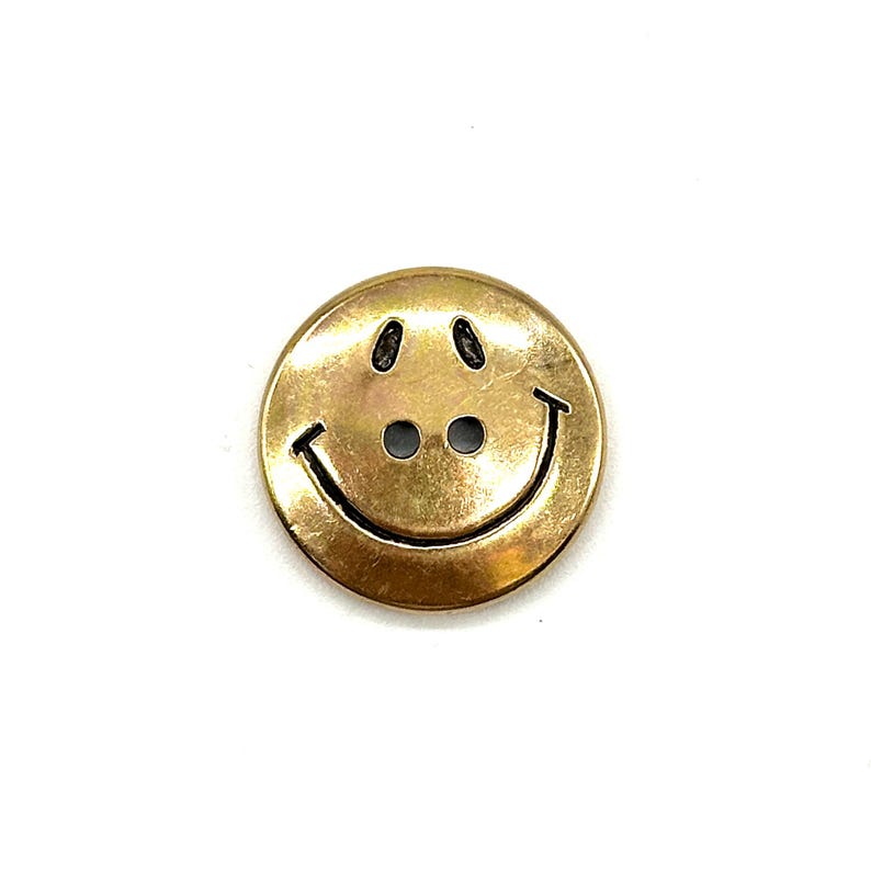 Pu&ograve; includere: Un bottone sorridente color oro con due fori per cucire. Il bottone &egrave; rotondo e ha una finitura lucida.