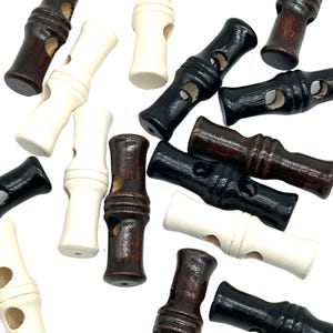 Puede incluir: Una colección de botones de madera de palanca en marrón, negro y blanco. Los botones son cilíndricos con un agujero en el centro y una ranura alrededor del medio.