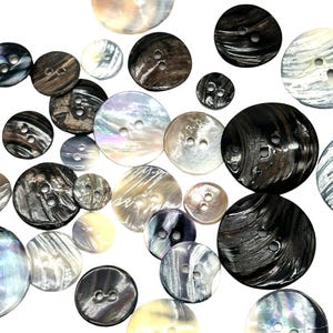May include: Assortment of round, two-hole buttons in various colours and patterns, including black, white, brown, and iridescent. The buttons are made of a smooth, shiny material.