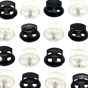 Könnte beinhalten: Ein Set mit 12 Toggle-Kordelverschlüssen, 6 schwarz und 6 klar. Die Kordelverschlüsse haben zwei Löcher und einen Federmechanismus.