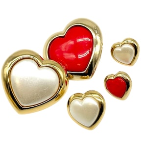 May include: Set of four heart-shaped earrings with gold frames. Two earrings feature a white pearl-like center, and two earrings feature a red center.
