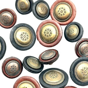 May include: A collection of decorative buttons with a gold and brown finish. The buttons have a raised design with a circular pattern in the centre. The buttons are scattered on a white background.