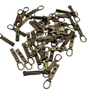 May include: A pile of antique gold-toned metal zipper pulls with a small loop at the top and two black dots on each pull.