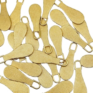 Puede incluir: Un grupo de 20 tiradores de cremallera de color dorado con una superficie texturizada. Los tiradores tienen forma de lágrima con un pequeño bucle en la parte superior.