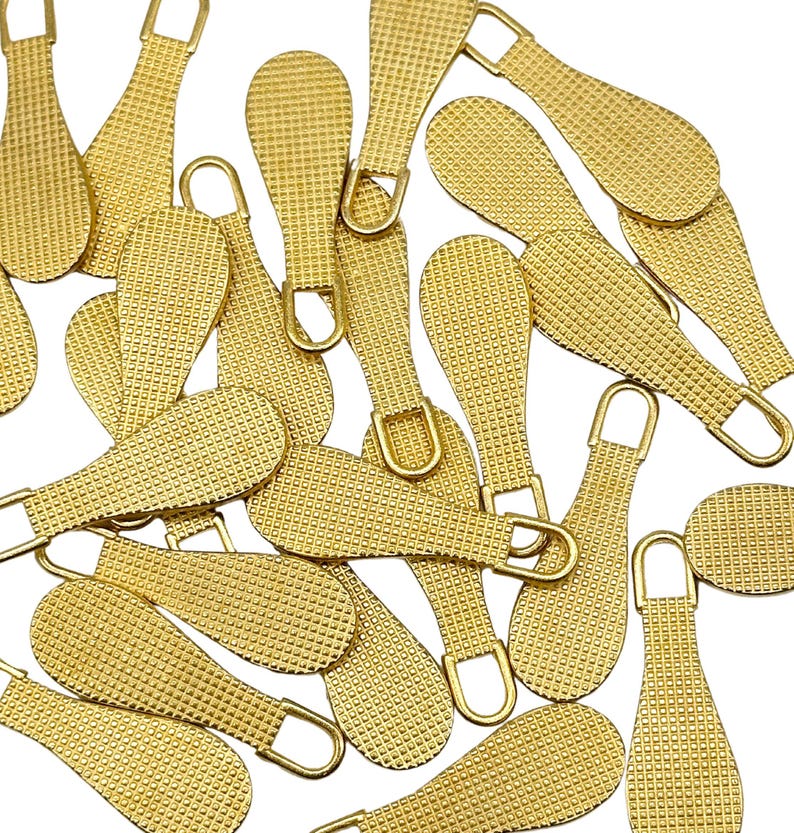 May include: A group of 20 gold-colored zipper pulls with a textured surface. The pulls are shaped like a teardrop with a small loop at the top.