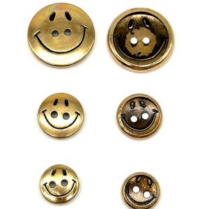 Pu&ograve; includere: Set di sei bottoni a forma di smiley dorati. I bottoni sono di diverse dimensioni e hanno una finitura lucida.