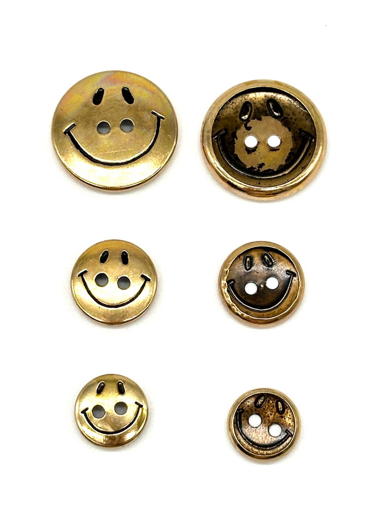 Pu&ograve; includere: Set di sei bottoni a forma di smiley dorati. I bottoni sono di diverse dimensioni e hanno una finitura lucida.