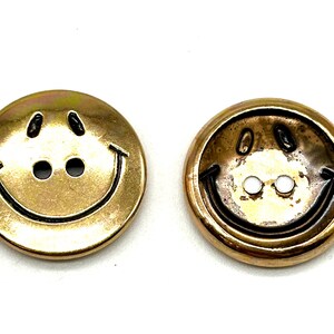 Pu&ograve; includere: Due bottoni dorati a forma di smiley con contorno nero. I bottoni hanno due fori per la cucitura.