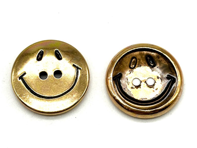 Pu&ograve; includere: Due bottoni dorati a forma di smiley con contorno nero. I bottoni hanno due fori per la cucitura.