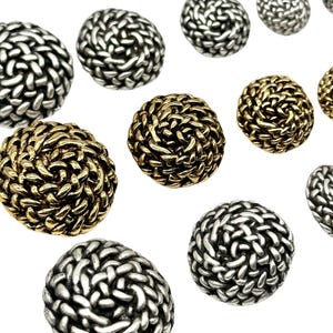 May include: A collection of decorative buttons with a woven design. The buttons are available in two colours: silver and gold.