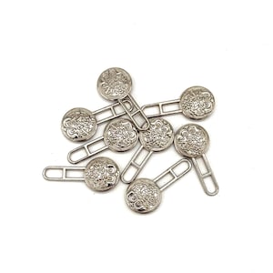 May include: A set of eight silver-toned metal button closures with decorative floral designs. Each closure has a round button with a metal loop on the back.