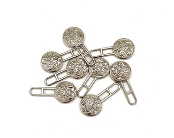 May include: A set of eight silver-toned metal button closures with decorative floral designs. Each closure has a round button with a metal loop on the back.