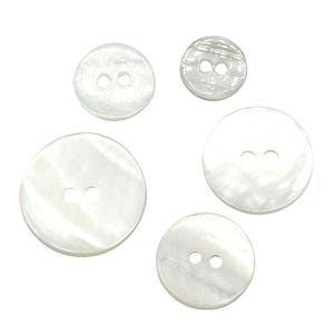 May include: Five white mother of pearl buttons of different sizes. The buttons are round and have two holes.