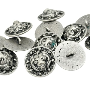 May include: A set of ten silver-toned metal buttons featuring a lion head design. The buttons have a textured surface and a loop on the back for sewing.