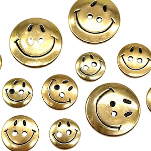 Pu&ograve; includere: Assortimento di bottoni con faccine sorridenti dorati di varie dimensioni. I bottoni hanno contorni neri e due occhi neri.