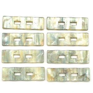 May include: Eight rectangular mother of pearl buttons with two rectangular holes each. The buttons are a light beige color with iridescent blue and green hues.