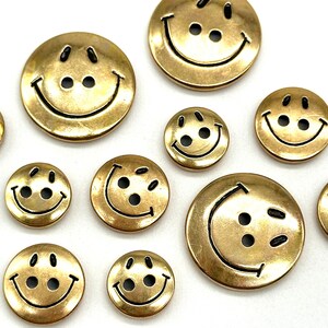Pu&ograve; includere: Assortimento di bottoni con faccine sorridenti dorati con contorni neri. I bottoni sono di varie dimensioni.